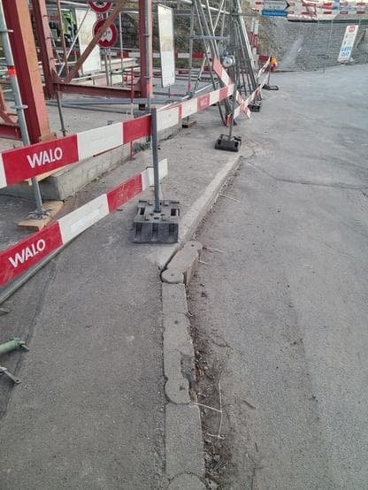 A narrow temporary ramp from the sidewalk in front of a concrete slab that goes across the sidewalk. There is construction site fencing around the slab, making the ramp inaccessible.
